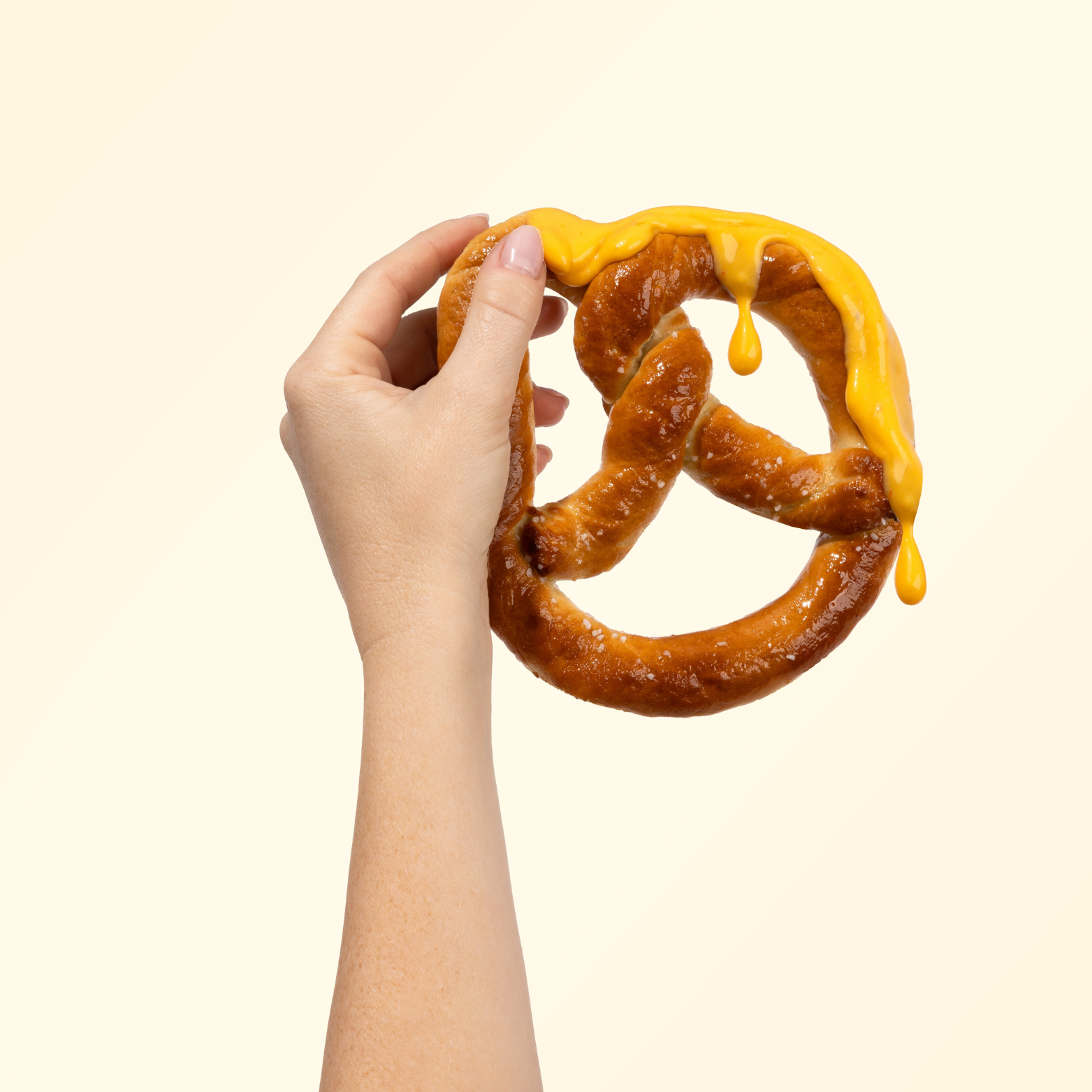 Hand holding a pretzel with cheese sauce on a beige background