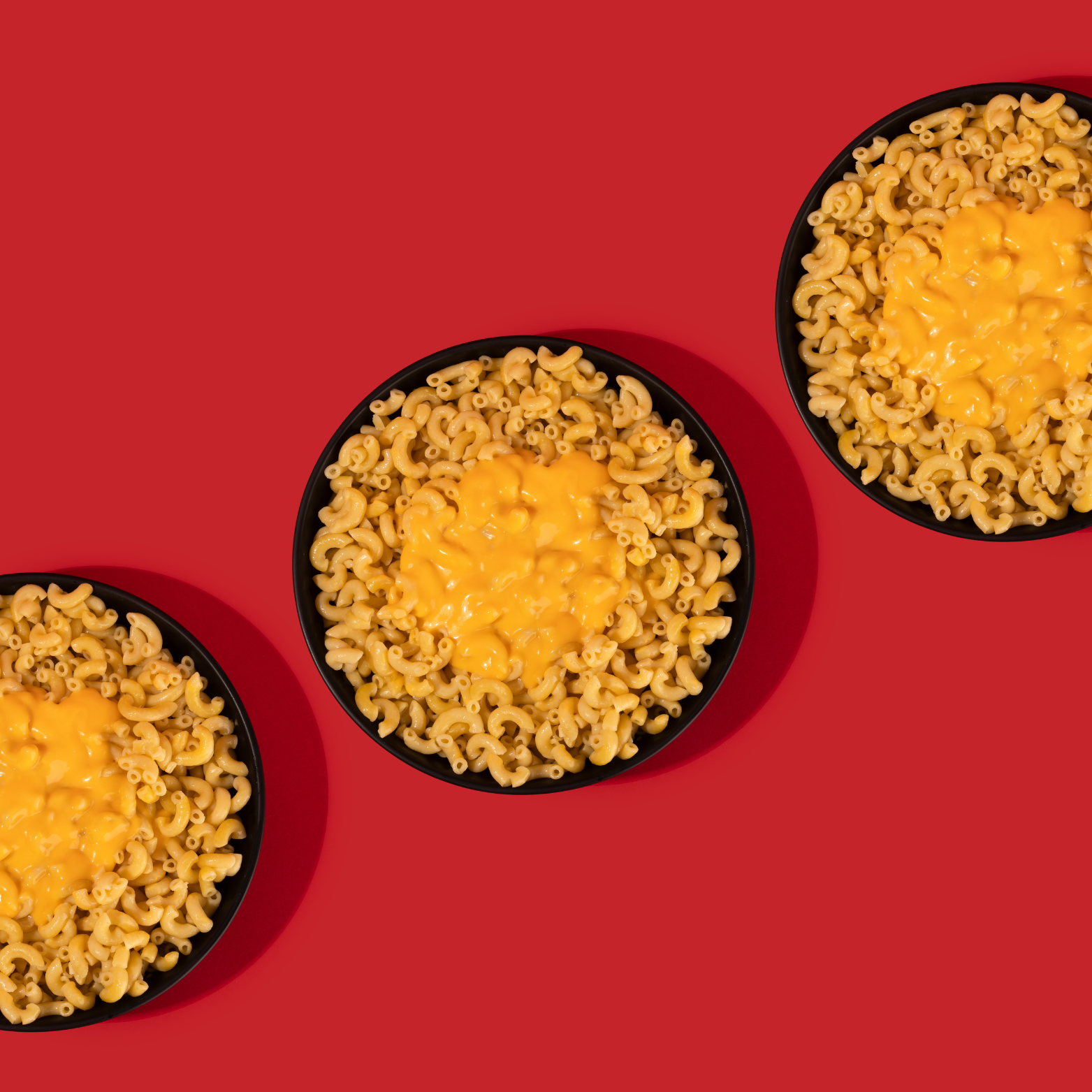 Three bowls of macaroni and cheese on a red background