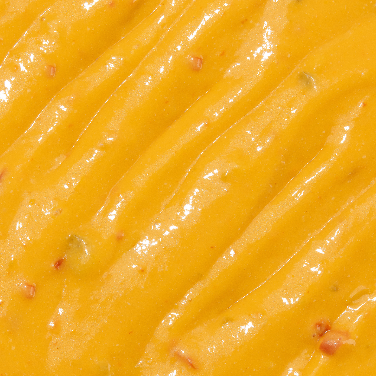 Close-up of a smooth, yellow sauce with small red and green specks.